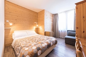Una habitación con paredes de paneles de madera, una cama con colcha estampada, una mesita de noche, un aparador, un sofá gris y una ventana con cortinas.