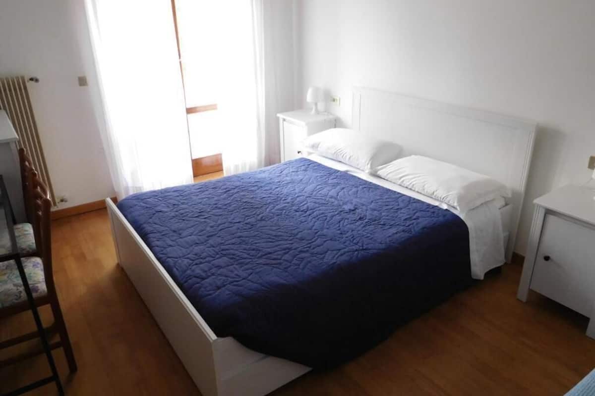 A bedroom with a bed, a nightstand, a chair, and a window with curtains.
