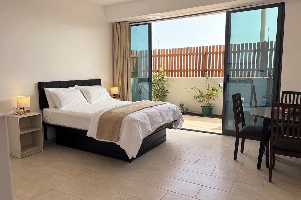 A hotel room with a bed, bedside table, lamp, and a view of the outdoor balcony.