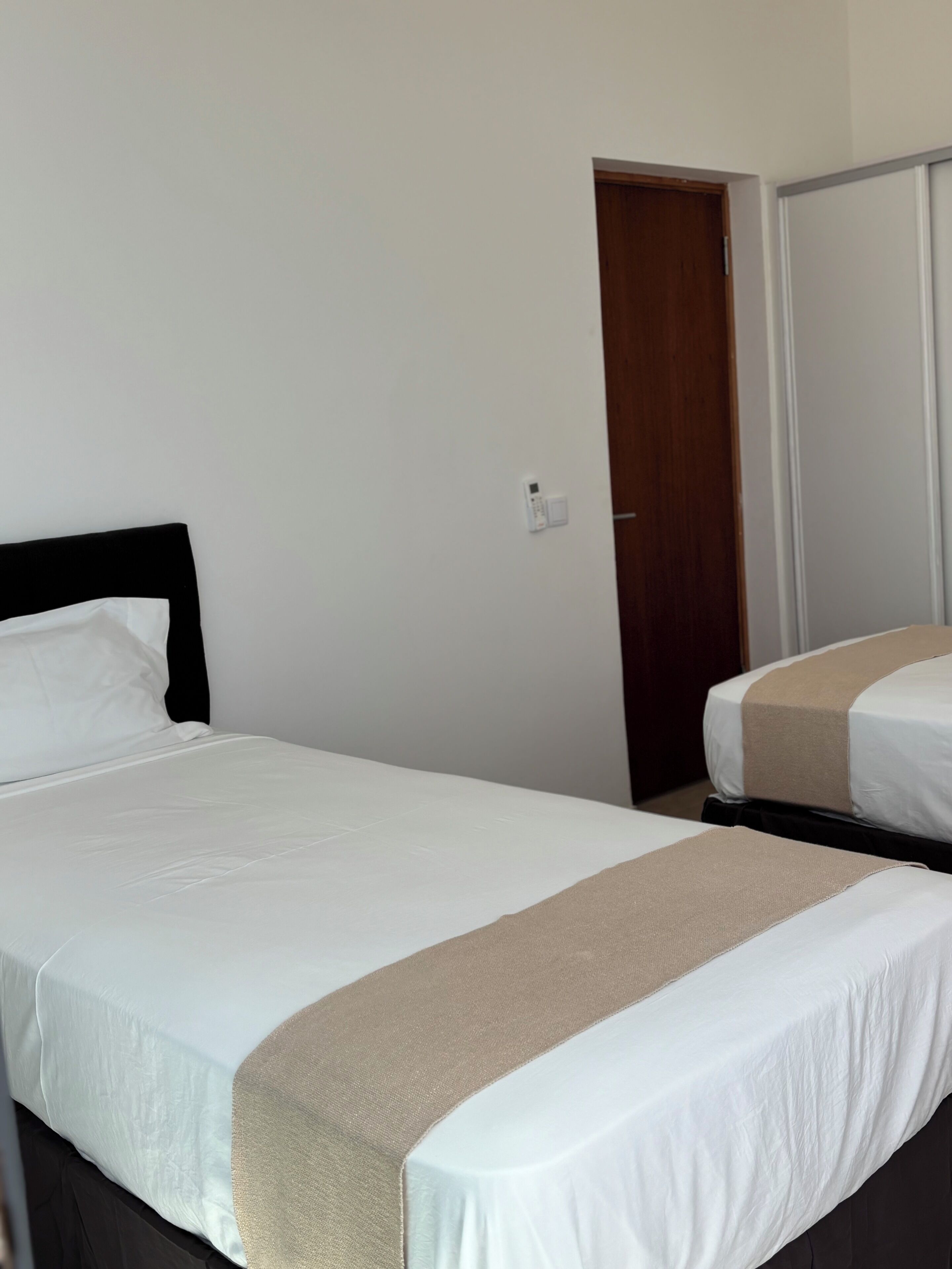 Ein Hotelzimmer mit zwei Einzelbetten, einer Holztür und einer weißen Wand.