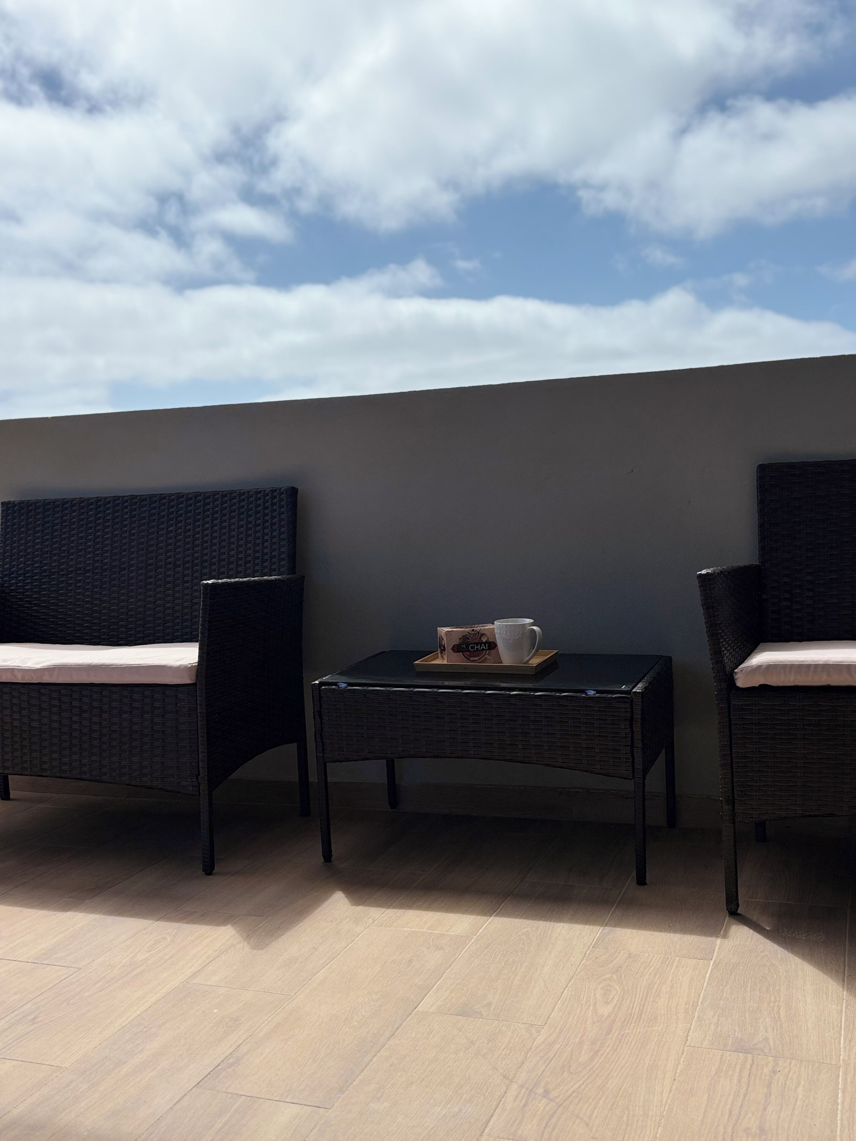 A balcony with wicker furniture, a small table, and a box of chai tea.