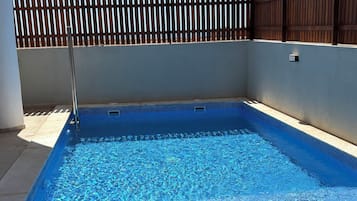 A swimming pool with a wooden fence, a sun lounger, and a hat on the lounger.
