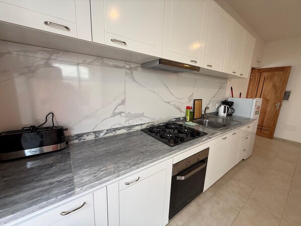 A modern kitchen with white cabinets, a marble backsplash, a gas stove, and a built-in oven.