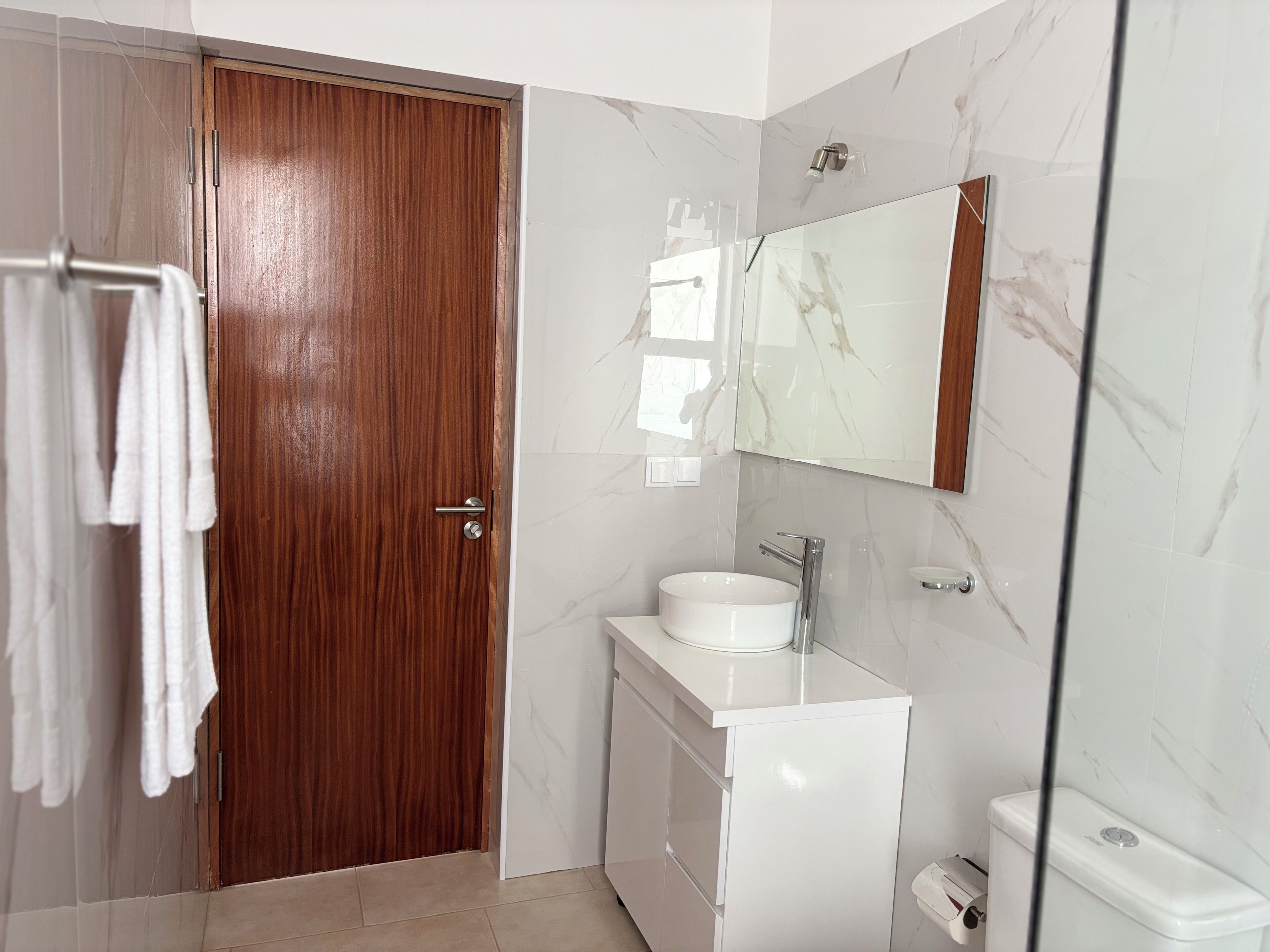 Ein Badezimmer mit Holztür, Waschbecken, Spiegel und Toilette.