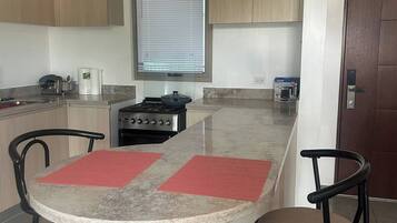 Una cocina moderna con una isla central, dos taburetes de bar, una estufa y una ventana con persianas.