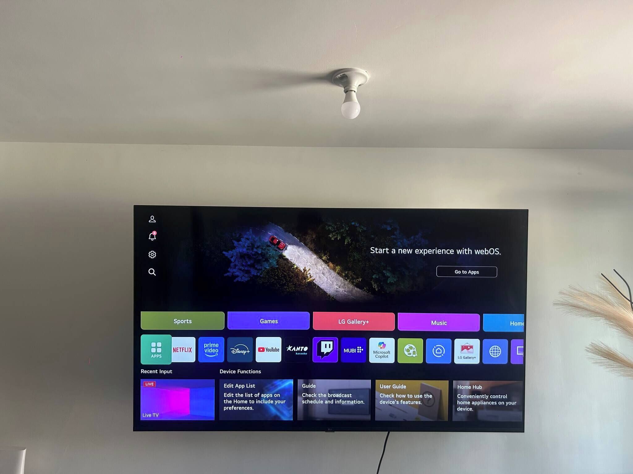 A TV mounted on a wall displaying a home screen with various app icons and a promotional message.