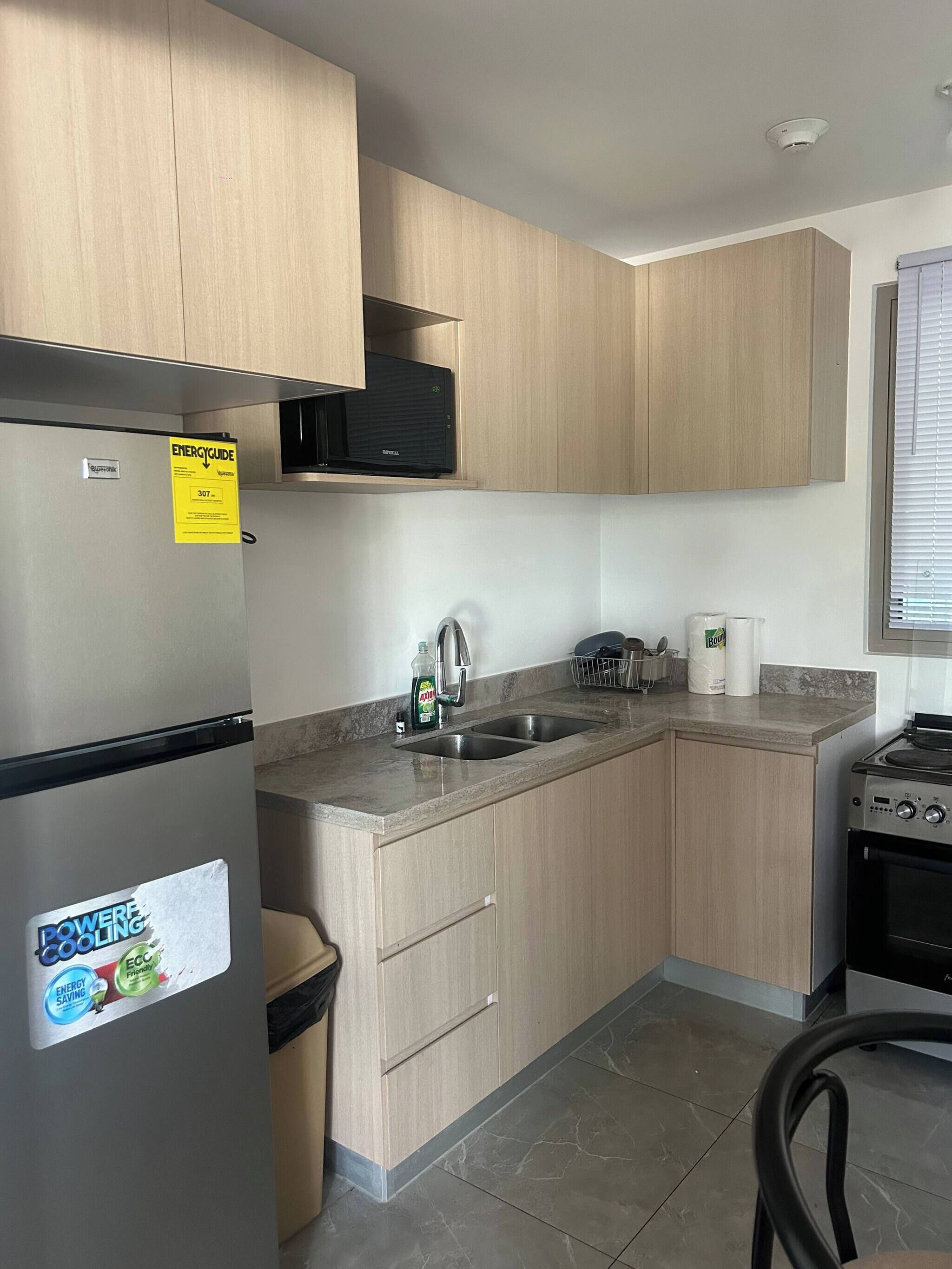 A modern kitchen with light wood cabinets, a stainless steel refrigerator, a microwave, and a stove.