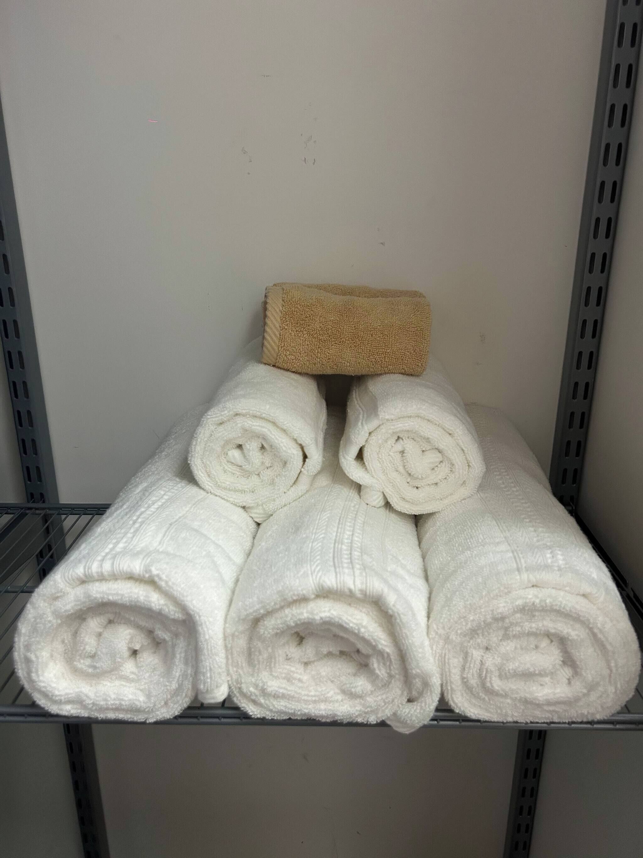 Une étagère avec des serviettes blanches pliées et un tapis de bain beige.