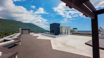 Terraza en la azotea con cubierta de madera, un edificio pequeño y montañas al fondo.