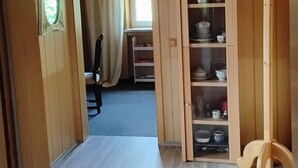 A wooden interior with a hallway leading to a room, a chandelier, and a cabinet with shelves.