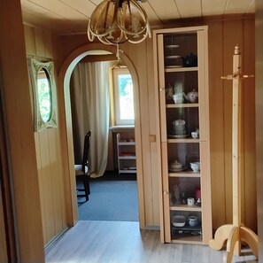 A wooden interior with a hallway leading to a room, a chandelier, and a cabinet with shelves.