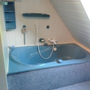Eine blaue Badewanne mit Duschkopf, Seifenschale und Handtuchhalter in einem Raum mit weißen Wänden und einer geneigten Decke.
