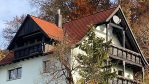 A two-story building with a red-tiled roof, balconies, and a garden area.