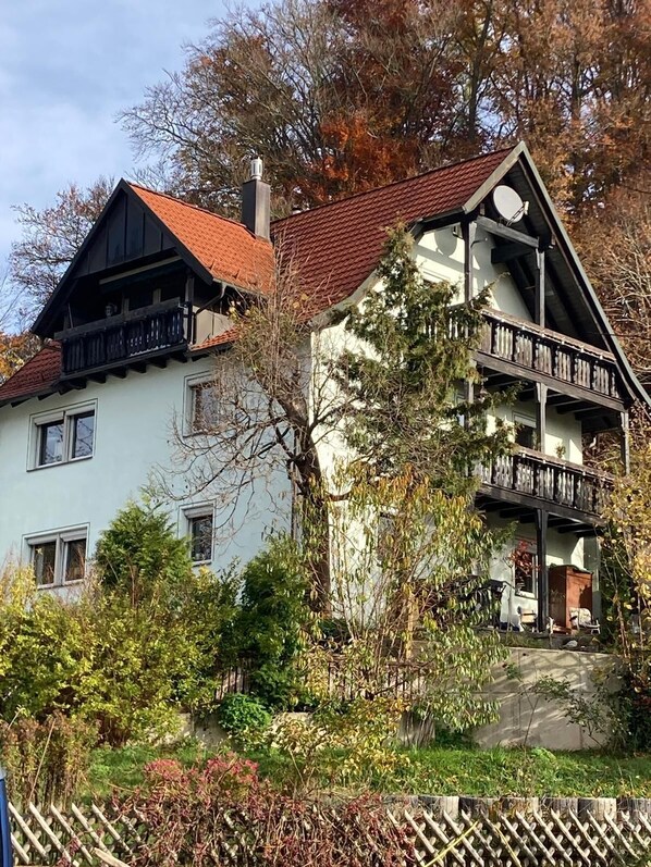 A two-story building with a red-tiled roof, balconies, and a garden area.