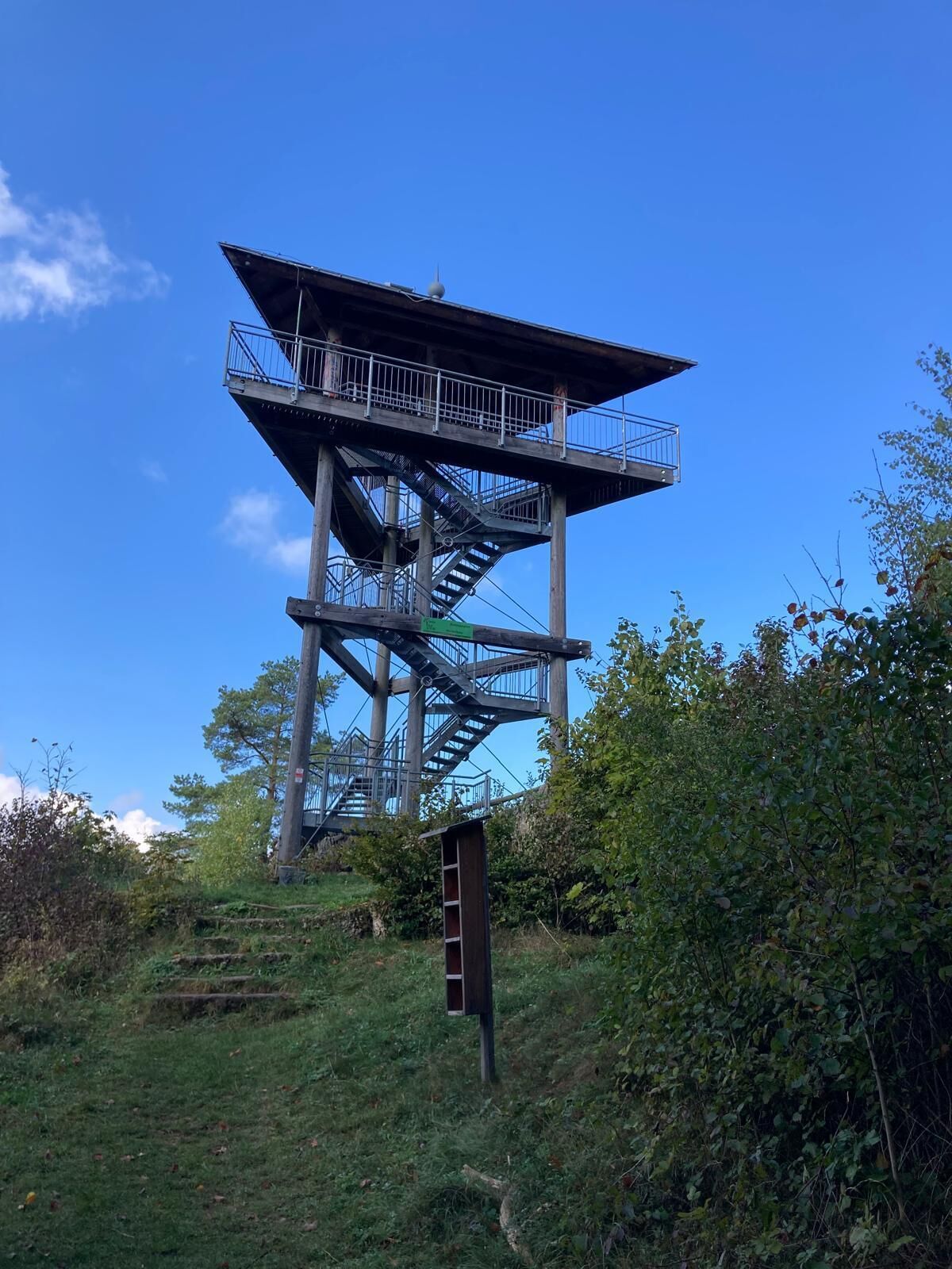 A tall observation tower with a metal staircase and a platform, surrounded by greenery.