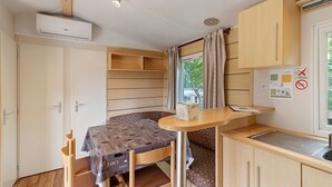 Een kleine keuken met een tafel, stoelen, een raam met gordijnen en een wandairconditioner.