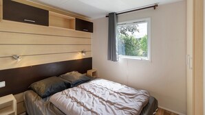 Een slaapkamer met een bed, nachtkastjes, een raam met gordijnen en inbouwplanken.