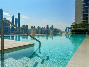 Una piscina con agua cristalina, una escalera metálica y el horizonte de la ciudad al fondo.