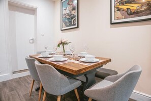 A dining area with a wooden table set for four, grey upholstered chairs, and framed artwork on the wall. - Gloucester-5 Bed Home for Work & Leisure (Gloucester)