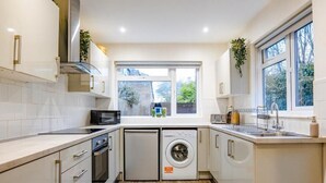 A modern kitchen with white cabinets, a built-in oven, a microwave, a dishwasher, and a window providing natural light. - Gloucester-5 Bed Home for Work & Leisure (Gloucester)