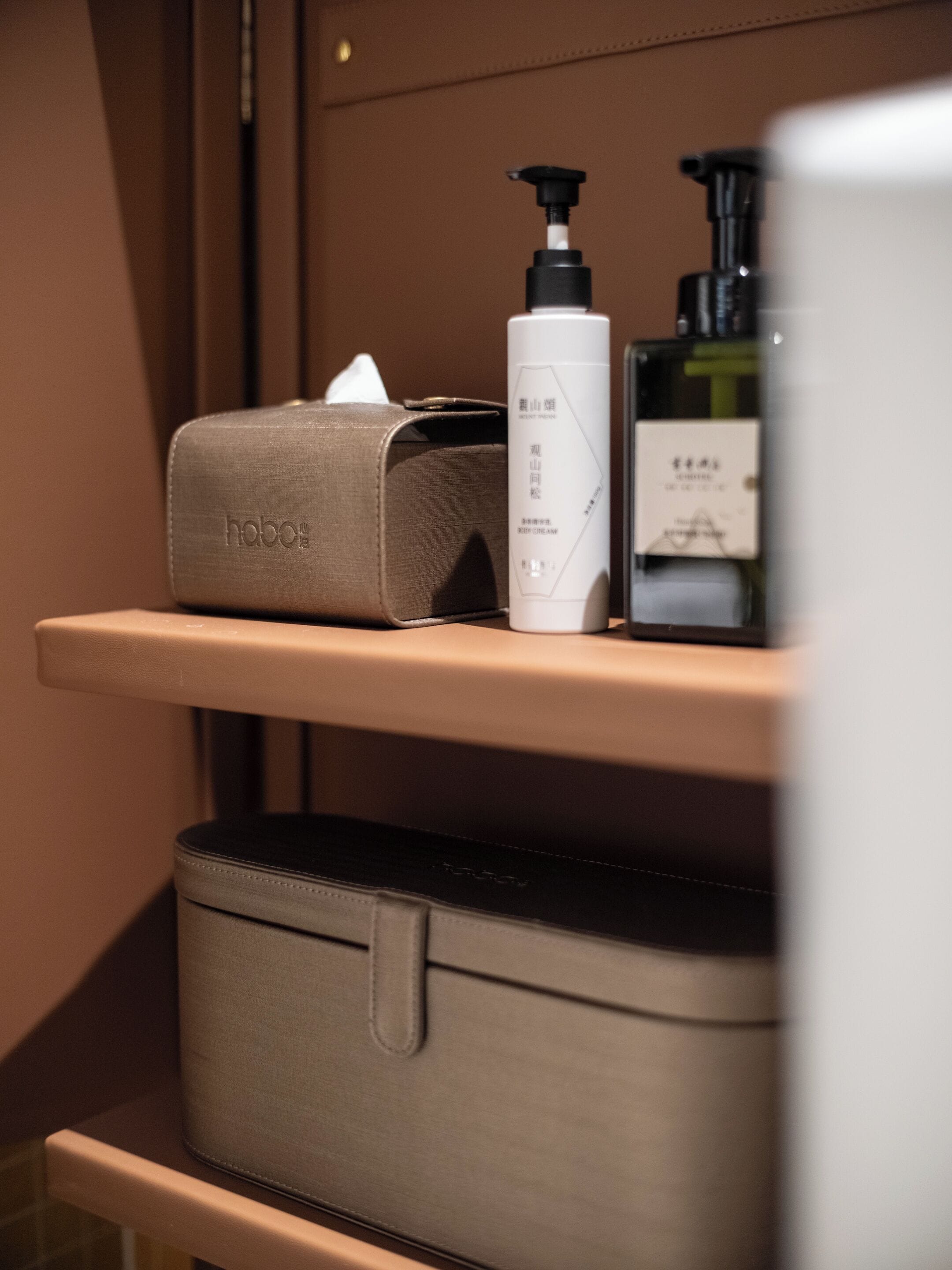 Un baño con una maleta color beige, una caja de pañuelos y dos botellas de loción sobre una repisa.