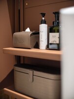 A bathroom with a beige suitcase, a tissue box, and two bottles of lotion on a shelf.