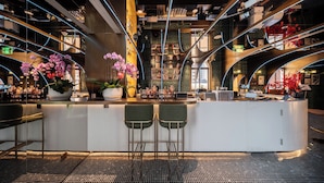 Un área de bar moderna con una barra curva, dos taburetes y una estantería llena de libros.