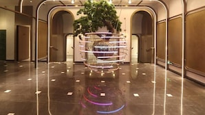 Un vestíbulo con un árbol decorativo central, piso reflectante y diseño de techo moderno.