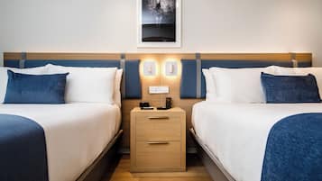 A hotel room with two beds, a nightstand with a phone and charger, and a framed picture on the wall.