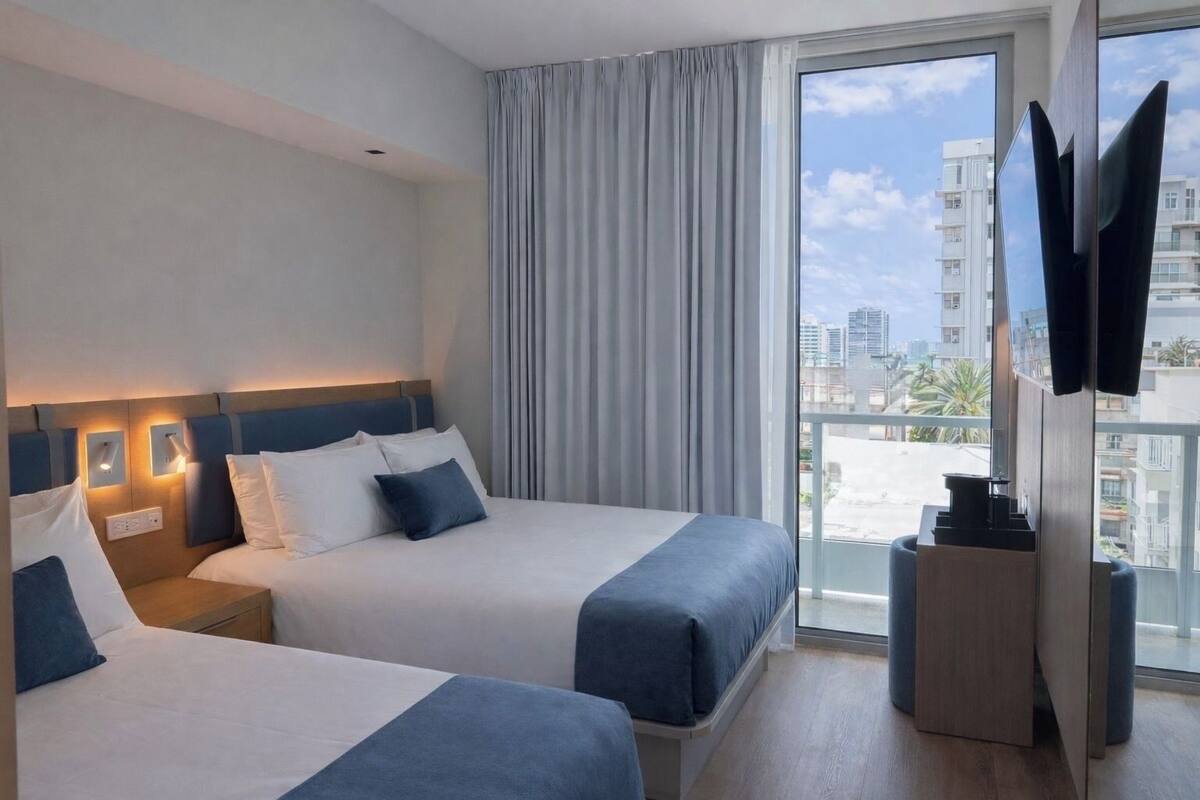 Ein Hotelzimmer mit zwei Betten, einem Fernseher und einem Balkon mit Blick auf die Stadt.