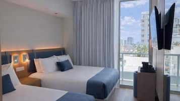 Habitación de hotel con dos camas, televisión y balcón con vista a la ciudad.