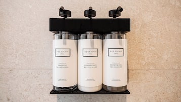Trois bouteilles de shampoing, d’après-shampoing et de gel douche de la marque Beekman 1802, posées sur une étagère.