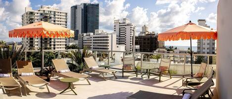 Terraza en la azotea con sillones de descanso y sombrillas, con vistas a un paisaje urbano lleno de edificios.