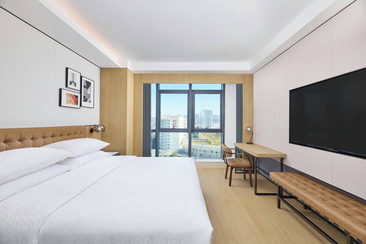 Une chambre d’hôtel moderne équipée d’un grand lit, d’un bureau, d’une banquette et d’un téléviseur.