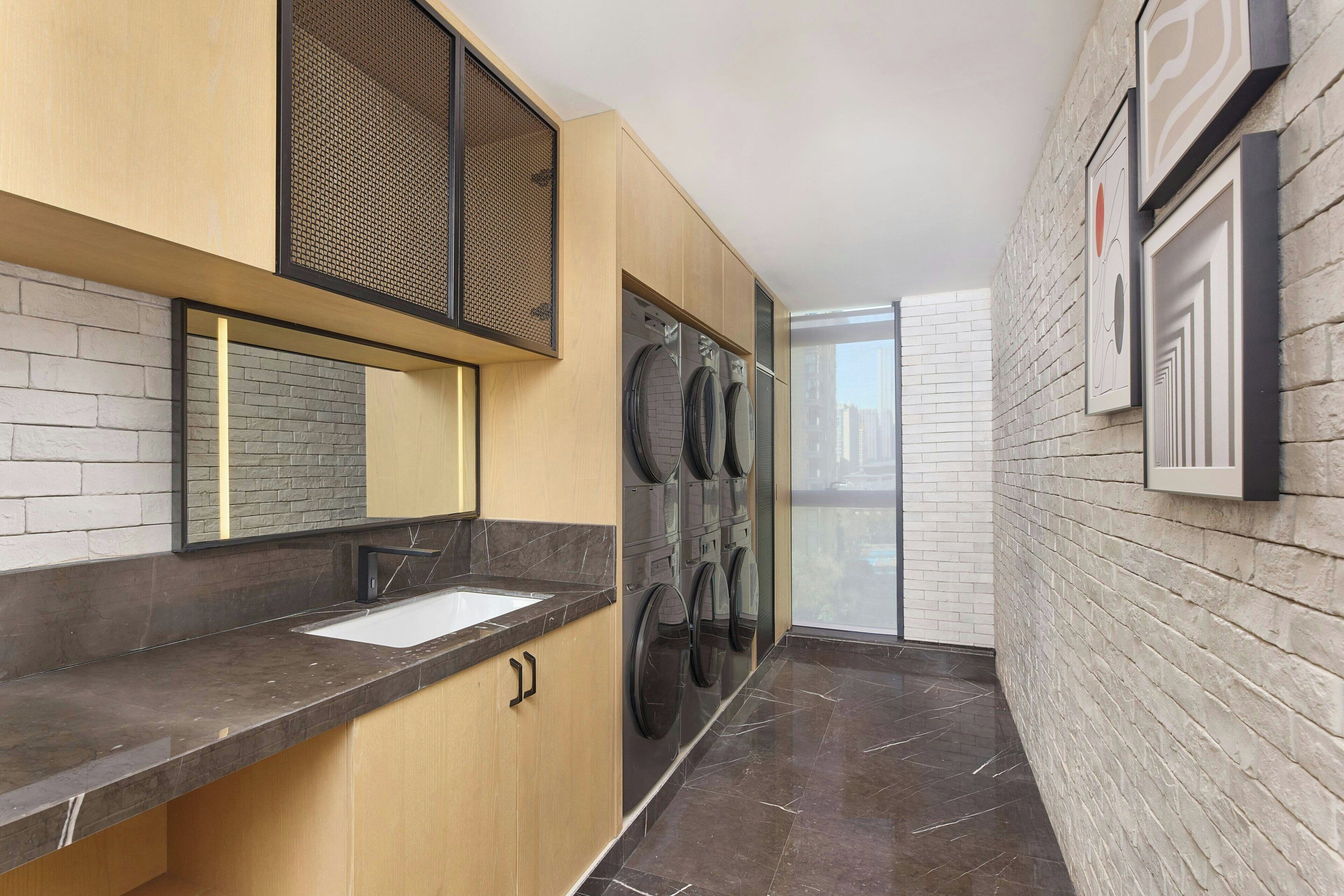 A modern laundry room with a sink, multiple washing machines, and a large window.