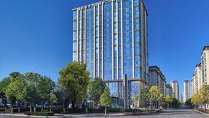 A modern high-rise hotel with a glass facade, multiple floors, and a clear sky. - Four Points by Sheraton Kunming Chenggong (Kunming)