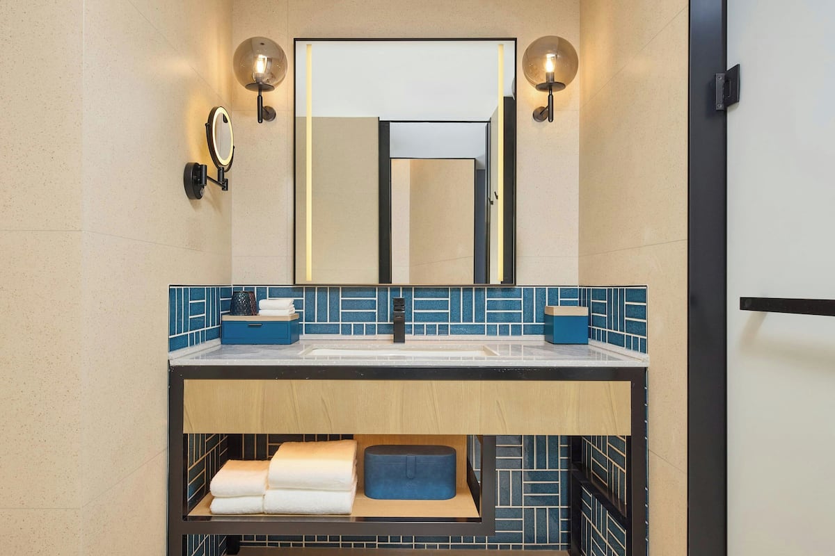 Une salle de bain moderne avec un grand miroir, deux appliques murales et un pare-chocs en carreaux bleus.