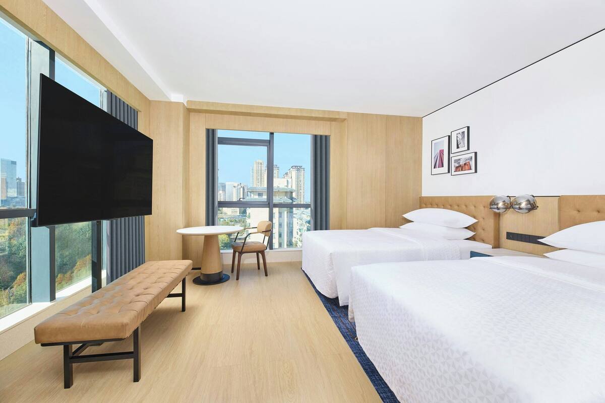 Une chambre d’hôtel avec deux lits, un banc, une table et un téléviseur.