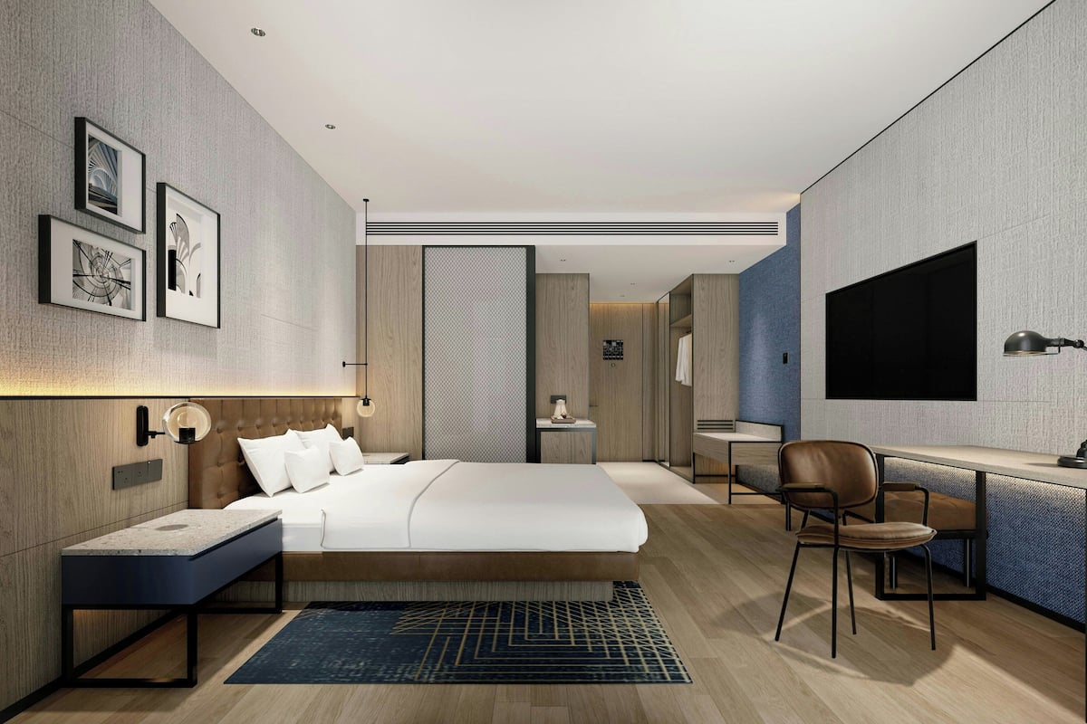 Une chambre d’hôtel moderne, dotée d’un grand lit, d’un bureau, d’une chaise et d’un téléviseur fixé au mur.