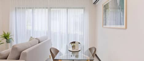Un salon moderne avec une table à manger en verre, un canapé beige et une plante en pot.