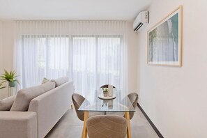 A modern living room with a glass dining table, beige sofa, and a potted plant. - Condominio Novatriana - SJO Airport (Alajuela)