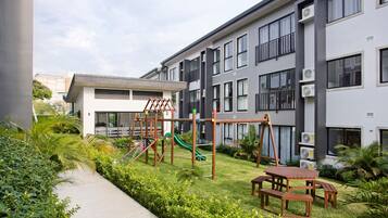 A modern apartment complex with a children's play area, including a slide and climbing structures.