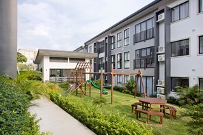 Un moderno complejo de apartamentos con área de juegos infantiles, que incluye un tobogán y estructuras para escalar.