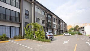 A multi-story parking garage with a modern design, featuring a car parked in the lot and a building with balconies and large windows in the background. - Condominio Novatriana - SJO Airport (Alajuela)