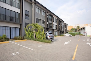 A multi-story parking garage with a modern design, featuring a car parked in the lot and a building with balconies and large windows in the background. - Condominio Novatriana - SJO Airport (Alajuela)