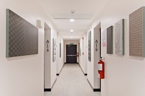 Un couloir d’hôtel avec des portes numérotées, un extincteur et un luminaire au plafond.