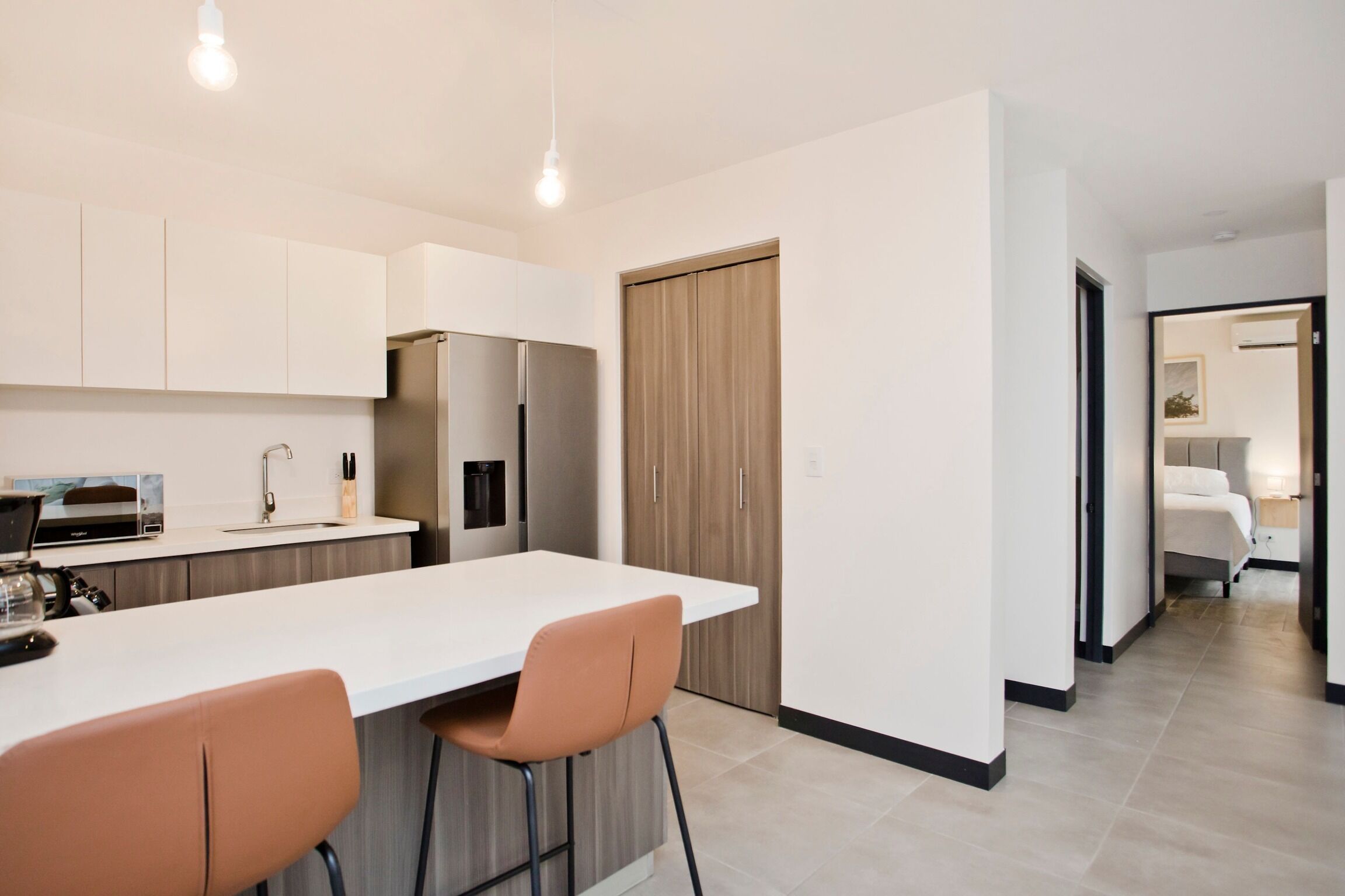 A modern kitchen with a central island, bar stools, a built-in oven, and a refrigerator.