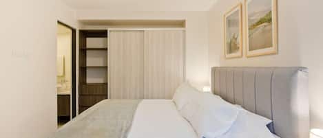 Ein Hotelzimmer mit Bett, Nachttisch, Kleiderschrank und einem durchgegangenen Tür sichtbaren Badezimmer.