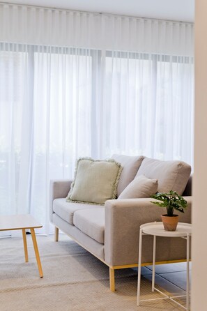 A living room with a sofa, a small table, and a potted plant. - Condominio Novatriana - SJO Airport (Alajuela)
