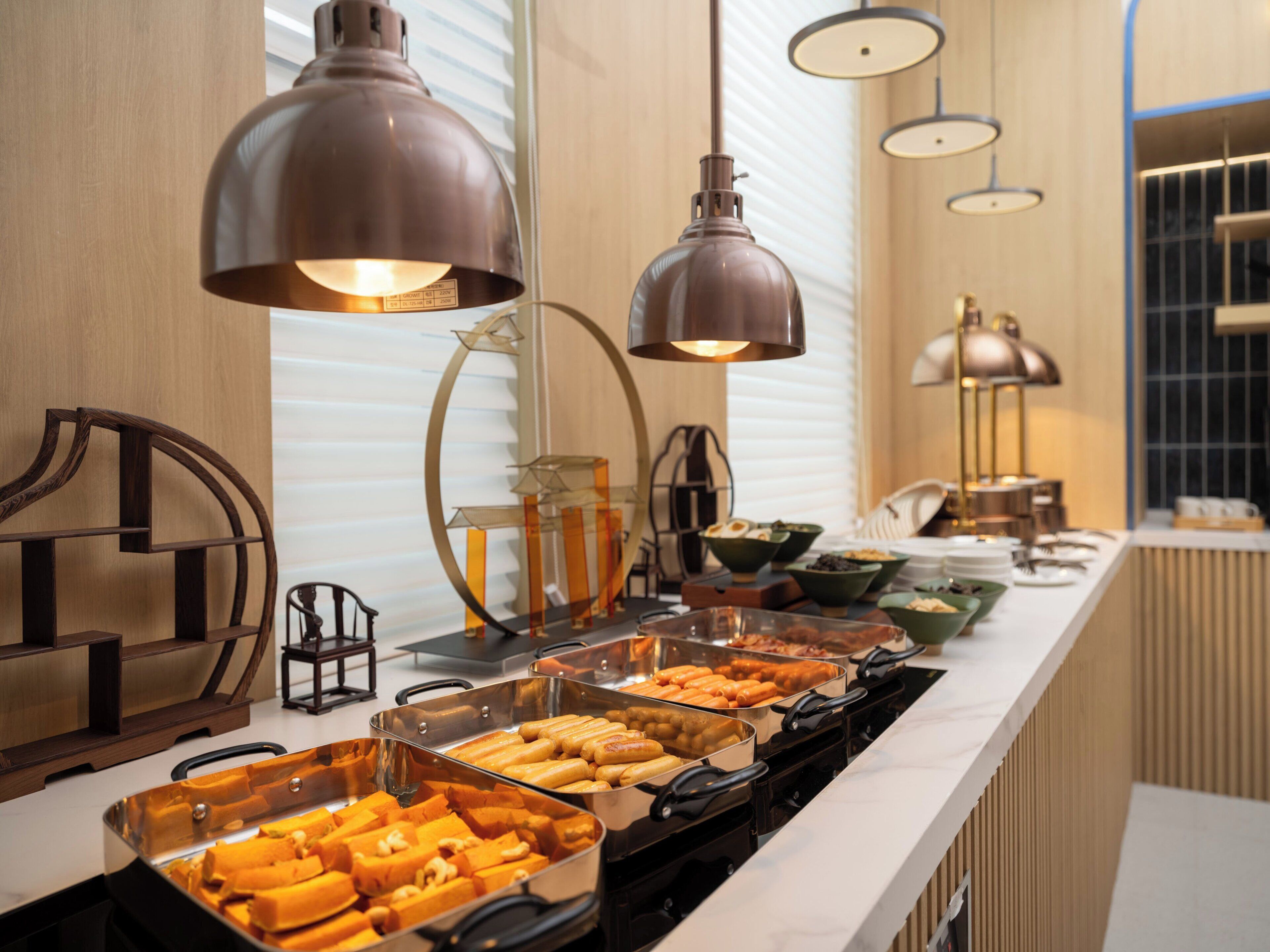 A buffet with various food items, overhead lighting, and a modern interior design.
